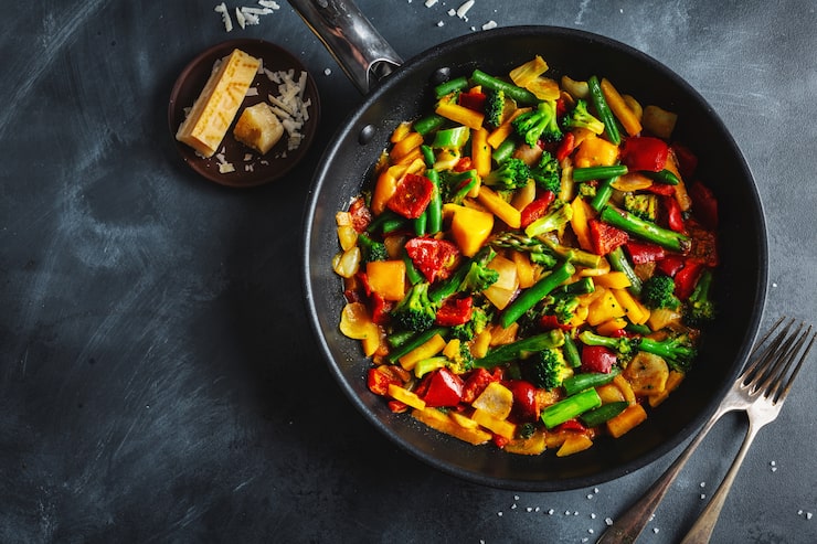 Poêlée de légumes sautés en sauce, poêle en fonte sur fond ardoise