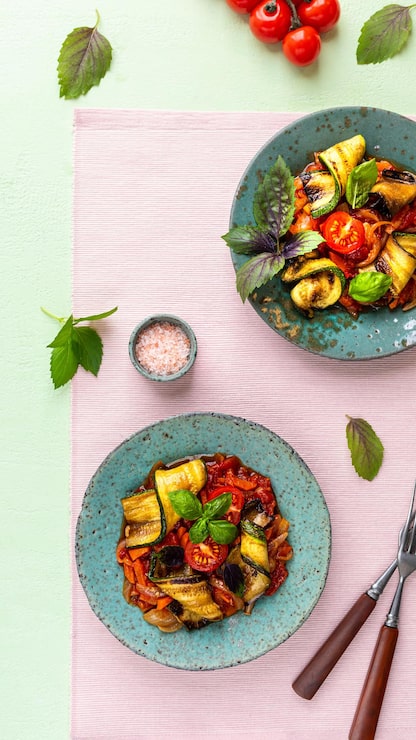 Deux assiettes turquoise de roulés de courgettes sautées aux carottes, oignons, ail et tomates