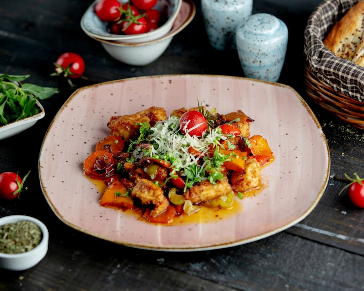 Assiette rose de poulet mijoté aux légumes, garni d'herbes, de parmesan et d'une tomate
