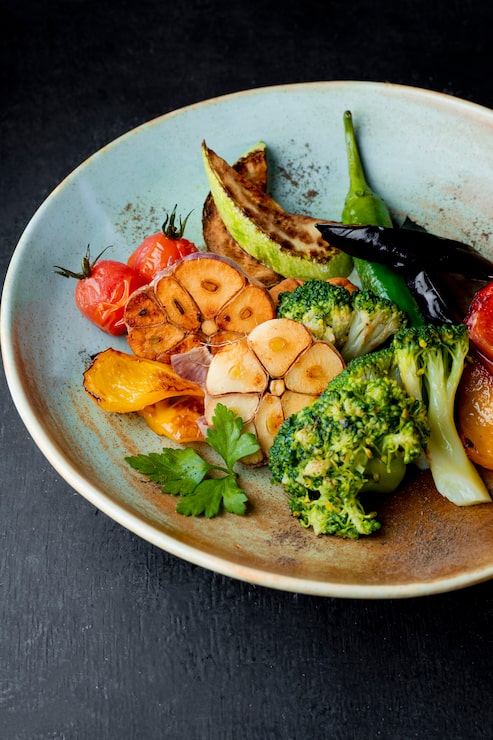 Gros plan de légumes grillés : brocoli, têtes d'ail confites, piments verts, tomates rôties