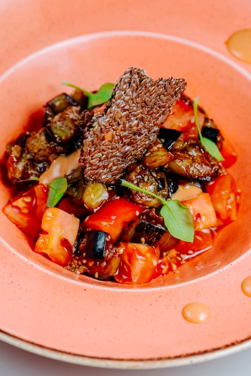 Caponata d'aubergines confites et tomates avec croustillant aux graines de lin, assiette corail