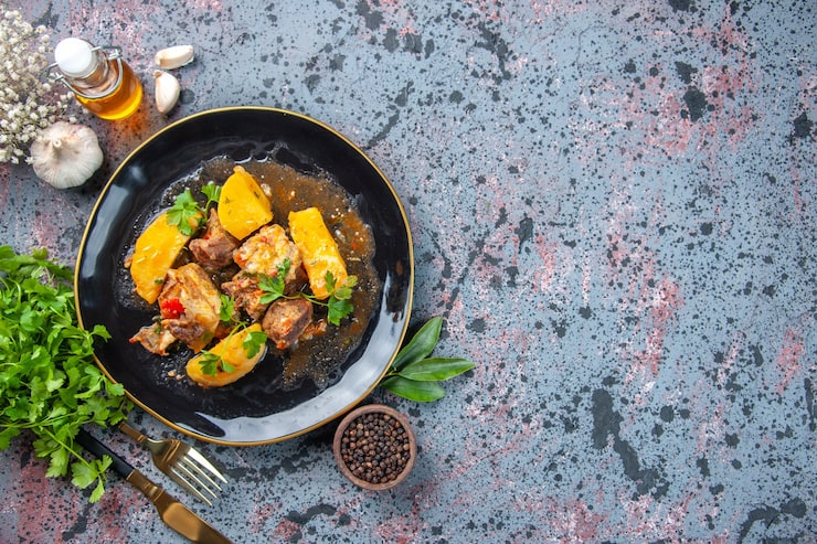 Assiette noire de viande en sauce et pommes de terre, servie avec huile d'olive, ail et poivre