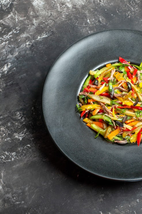 Tagliatelles de légumes croquants aux olives sur grande assiette sombre